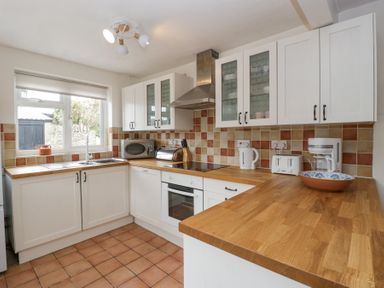 A kitchen with white cabinets wooden countertops a stove oven microwave toaster kettle coffee maker and a window at Spring Cottage in Birdlip near Brockworth
