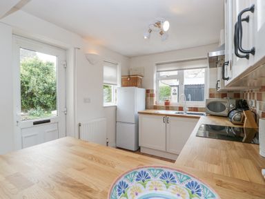 A kitchen with white cabinets wooden countertops a refrigerator a microwave and a view of a garden at Spring Cottage in Birdlip near Brockworth