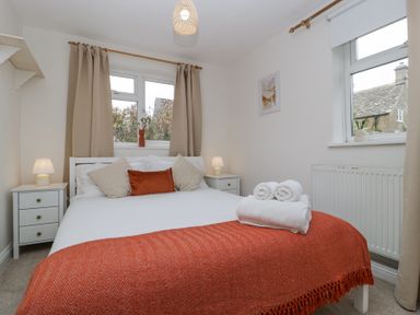 A bedroom with a bed pillows nightstands lamps and two windows at Spring Cottage Birdlip near Brockworth