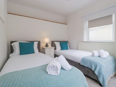 A bedroom with two single beds with teal cushions and throws towels on beds and a bedside table with lamp at Spring Cottage in Birdlip near Brockworth