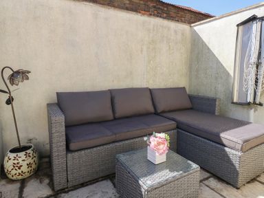 An outdoor seating area with a wicker sofa with cushions a glass top table with flowers and a decorative flower lamp at Seaside House in Weymouth