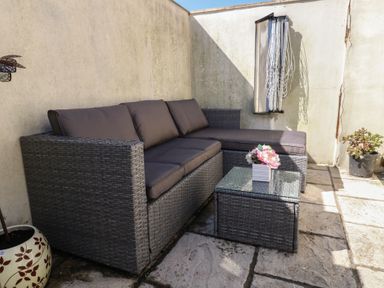 An outdoor patio area with a rattan sofa and coffee table with flowers and potted plants against a corner wall