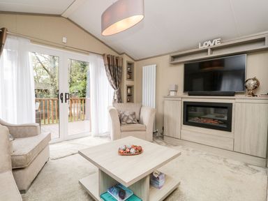 A living room with beige chairs a wooden coffee table a fireplace and a mounted TV at Water's Reach White Cross Bay Holiday Park near Troutbeck Bridge