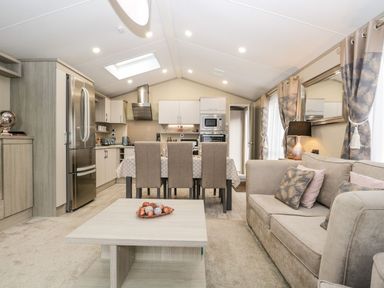 An open plan living room and kitchen with a sofa coffee table dining table and chairs at Water's Reach White Cross Bay Holiday Park near Troutbeck Bridge