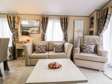A living room with a sofa armchair coffee table and curtains at Water's Reach White Cross Bay Holiday Park near Troutbeck Bridge