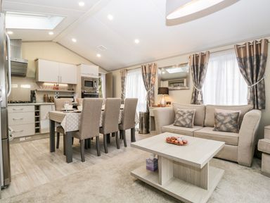 A combined kitchen and living area with dining table and chairs sofa coffee table and curtains at Water's Reach White Cross Bay Holiday Park near Troutbeck Bridge