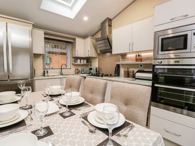 A kitchen with a dining table set for six people and modern appliances at Water's Reach White Cross Bay Holiday Park near Troutbeck Bridge