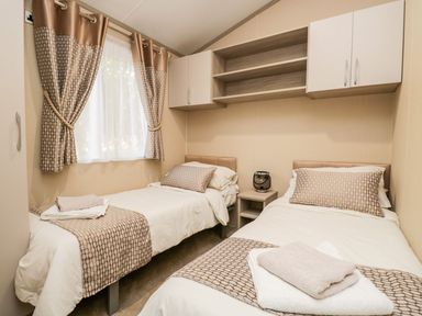 A bedroom with two single beds a nightstand with a lantern and wall cabinets at Waters Reach White Cross Bay Holiday Park near Troutbeck Bridge