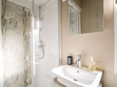 A bathroom with a shower area next to a sink with a faucet cup and soap dispenser at Water's Reach White Cross Bay Holiday Park near Troutbeck Bridge