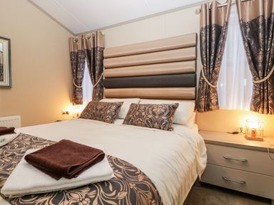 A bedroom with a bed with patterned pillows and folded towels on top at Water's Reach White Cross Bay Holiday Park near Troutbeck Bridge