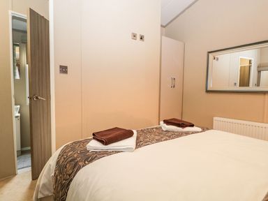 A bedroom with a bed topped with folded towels a wall mirror a door and a wardrobe at Water's Reach White Cross Bay Holiday Park near Troutbeck Bridge