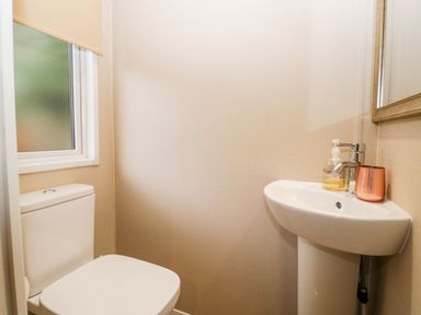 A small bathroom with a toilet next to a frosted window and a sink with hand soap and a cup at Water's Reach White Cross Bay Holiday Park near Troutbeck Bridge