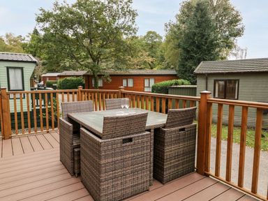 An outdoor deck with a glass top table and four wicker chairs surrounded by wooden railings at Water's Reach White Cross Bay Holiday Park near Troutbeck Bridge