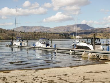 Boats moored at a floating dock on a lake with mountains in the background at Water's Reach White Cross Bay Holiday Park near Troutbeck Bridge