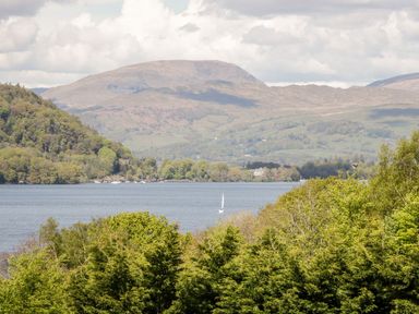 A lake with a sailboat surrounded by green trees and hills at Waters Reach White Cross Bay Holiday Park near Troutbeck Bridge