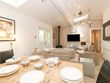 A dining table set with plates glasses and cutlery next to a living area with sofas a television and wood burner at Serenity Skiptory Howe 10 White Cross Bay near Windermere