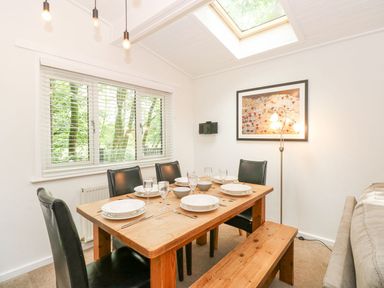 A dining room with a wooden table set for six with plates glasses cutlery black chairs a bench a window with blinds a floor lamp and a skylight at Serenity Skiptory Howe 10 White Cross Bay near Windermere
