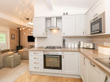 A kitchen with white cabinets a stove oven microwave kettle toaster and knife set along with a view into a living room at Serenity Skiptory Howe 10 White Cross Bay near Windermere