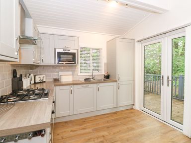 A kitchen with gray cabinets a gas stove a microwave a sink and glass doors opening to a deck at Serenity in Skiptory Howe 10 White Cross Bay near Windermere