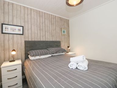 A bedroom with a double bed gray striped bedding two bedside tables with lamps and towels on the bed at Serenity Skiptory Howe 10 White Cross Bay near Windermere