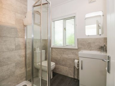 A bathroom with a shower enclosure a toilet a sink with a cabinet a wall mirror and a window with blinds at Serenity Skiptory Howe 10 White Cross Bay near Windermere