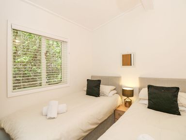A bedroom with two single beds a bedside table with a lamp and a window with blinds at Serenity Skiptory Howe 10 White Cross Bay near Windermere