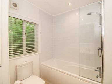 A bathroom with a bathtub with a shower head and a toilet near a window with blinds at Serenity Skiptory Howe 10 White Cross Bay near Windermere