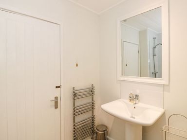 A bathroom with a sink a mirror a silver towel rack a door and a shower visible in the mirror at Serenity Skiptory Howe 10 White Cross Bay near Windermere