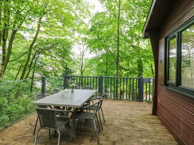 A wooden deck with a table and six chairs surrounded by trees at Serenity Skiptory Howe 10 White Cross Bay near Windermere
