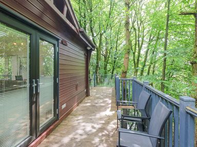 A wooden deck with two chairs and a small table next to a building surrounded by trees at Serenity Skiptory Howe 10 White Cross Bay near Windermere