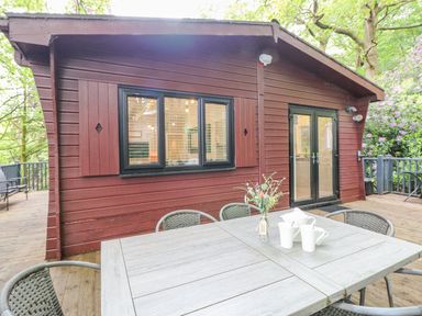 An outdoor dining table with flower vase and cups on a wooden deck next to a red wooden cabin at Serenity Skiptory Howe 10 White Cross Bay near Windermere