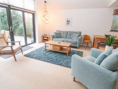 A living room with blue sofas a wooden coffee table and sliding glass doors at Chy Benyngoth in Hayle