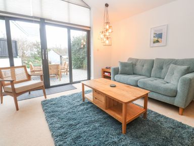 A living room with a green sofa a wooden coffee table a blue rug and large sliding glass doors at Chy Benyngoth in Hayle