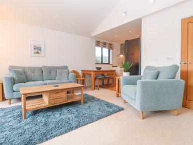 A living room with two blue sofas a wooden coffee table a dining table with chairs and a window at Chy Benyngoth in Hayle