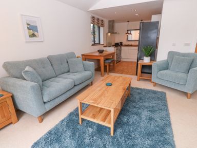 A living room with two blue sofas a wooden coffee table and a blue rug near a kitchen at Chy Benyngoth in Hayle