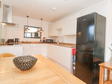 A kitchen with white cabinets black fridge wooden countertops and a wooden table with a black bowl at Chy Benyngoth in Hayle