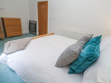 A bedroom with a bed that has pillows and a blanket a wooden dresser a wooden door and a radiator at Chy Benyngoth in Hayle
