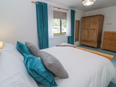 A bedroom with a bed with blue and gray pillows a window with blue curtains a wooden wardrobe and a chest of drawers at Chy Benyngoth in Hayle