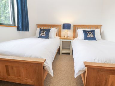 A bedroom with two single beds with wooden frames white bedding and blue bee cushions at Chy Benyngoth in Hayle
