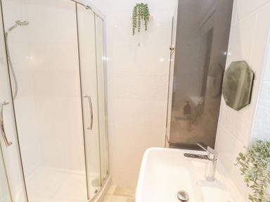 A bathroom with a shower enclosure a sink with a faucet and plants at Chy Benyngoth in Hayle