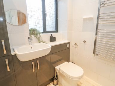 A bathroom with a sink cabinet, toilet, towel rack, and small window at Chy Benyngoth in Hayle
