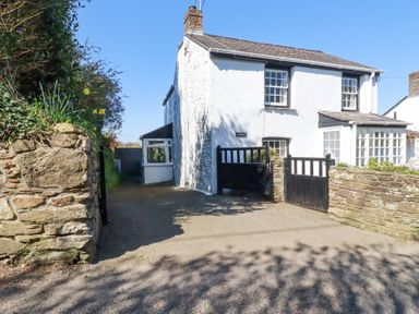 A white two story house with a black gate and stone walls in front at Pennine in Veryan