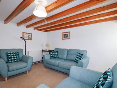 A sitting room with blue armchairs and a sofa with patterned cushions under wooden ceiling beams at Pennine in Veryan