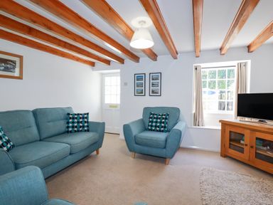 A living room with blue sofas and a wooden TV stand under exposed wooden ceiling beams at Pennine in Veryan