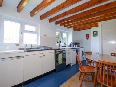 A kitchen with wooden beams on the ceiling a table with chairs and appliances at Pennine in Veryan