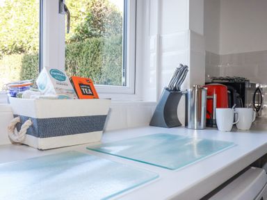 A kitchen countertop with a window basket containing tea and biscuits knives in a stand a red kettle two white mugs and a coffee press at Pennine in Veryan