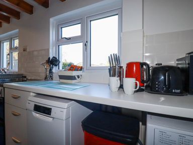 A kitchen countertop with a red kettle black toaster white mugs knife block and a basket with tea bags at Pennine in Veryan