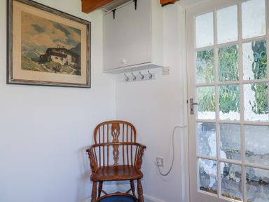 A wooden chair under a framed painting on a white wall next to a glass-panel door at Pennine in Veryan
