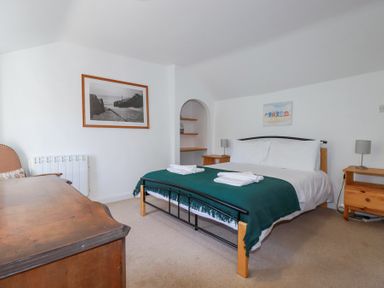 A bedroom with a bed covered by a green blanket and white pillows beside wooden nightstands and a wooden dresser at Pennine in Veryan