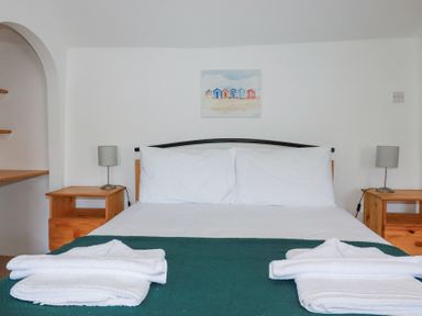A bedroom with a bed with white linens two bedside tables with lamps and folded towels at Pennine in Veryan
